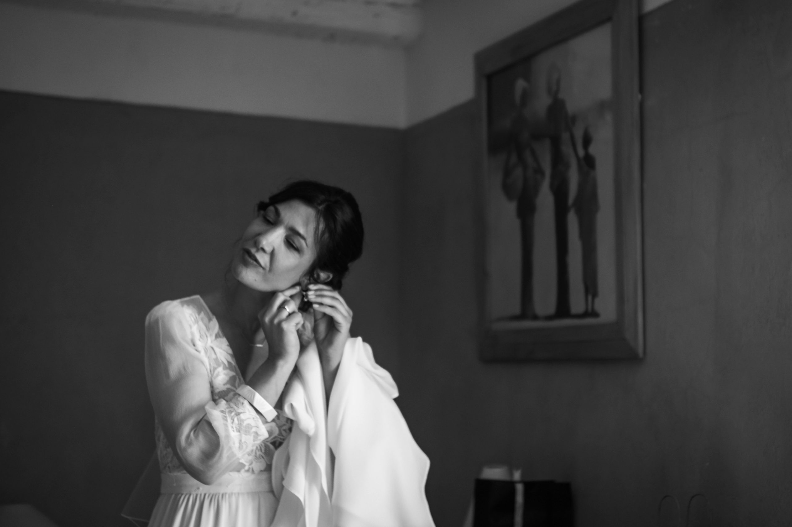 La mariée met ses boucles d'oreilles, dernier geste des préparatifs avant la cérémonie, en noir et blanc