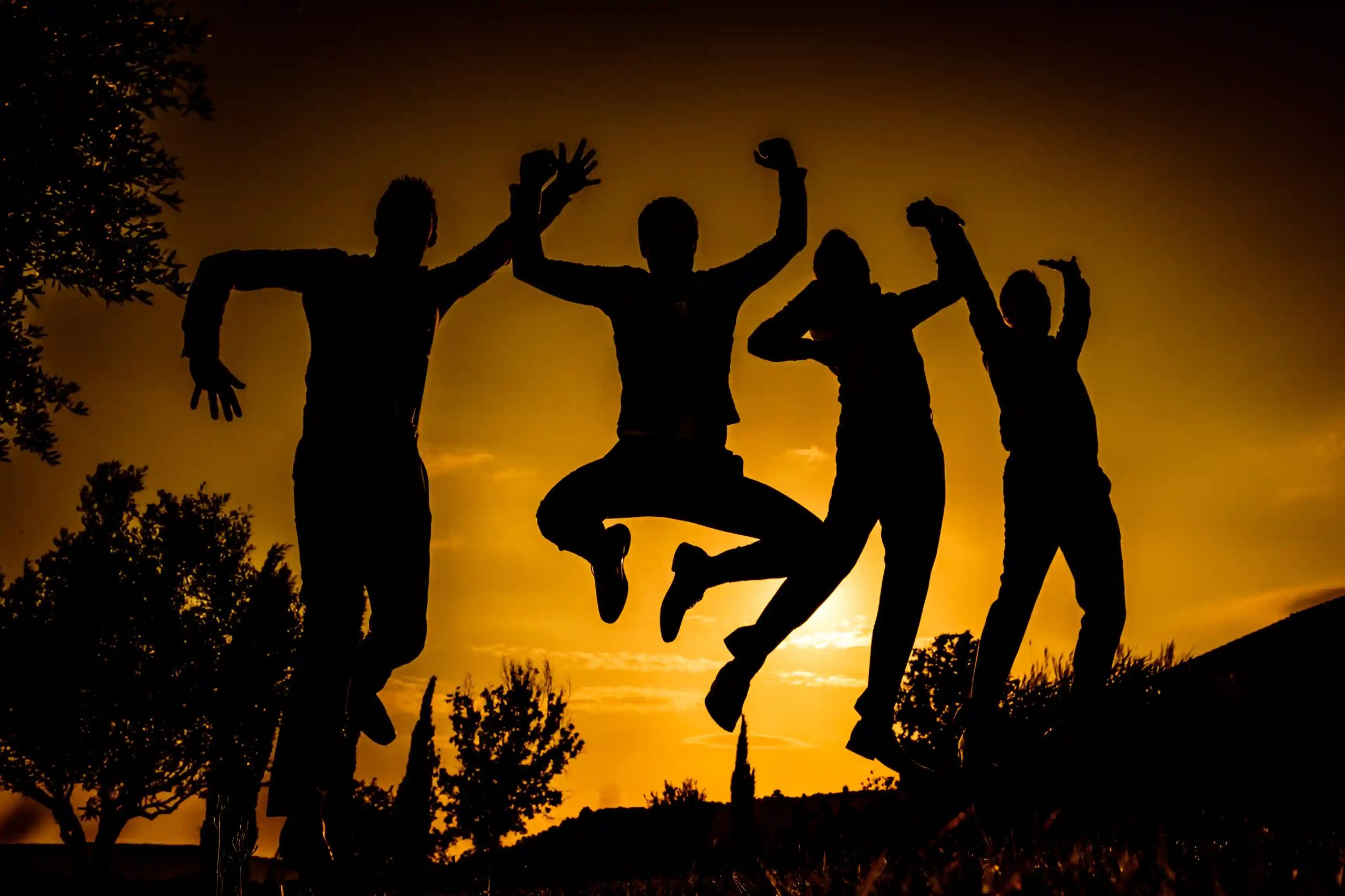 groupe d'amis qui sautent ensemble en silhouette au coucher du soleil pour une photo de groupe rigolote