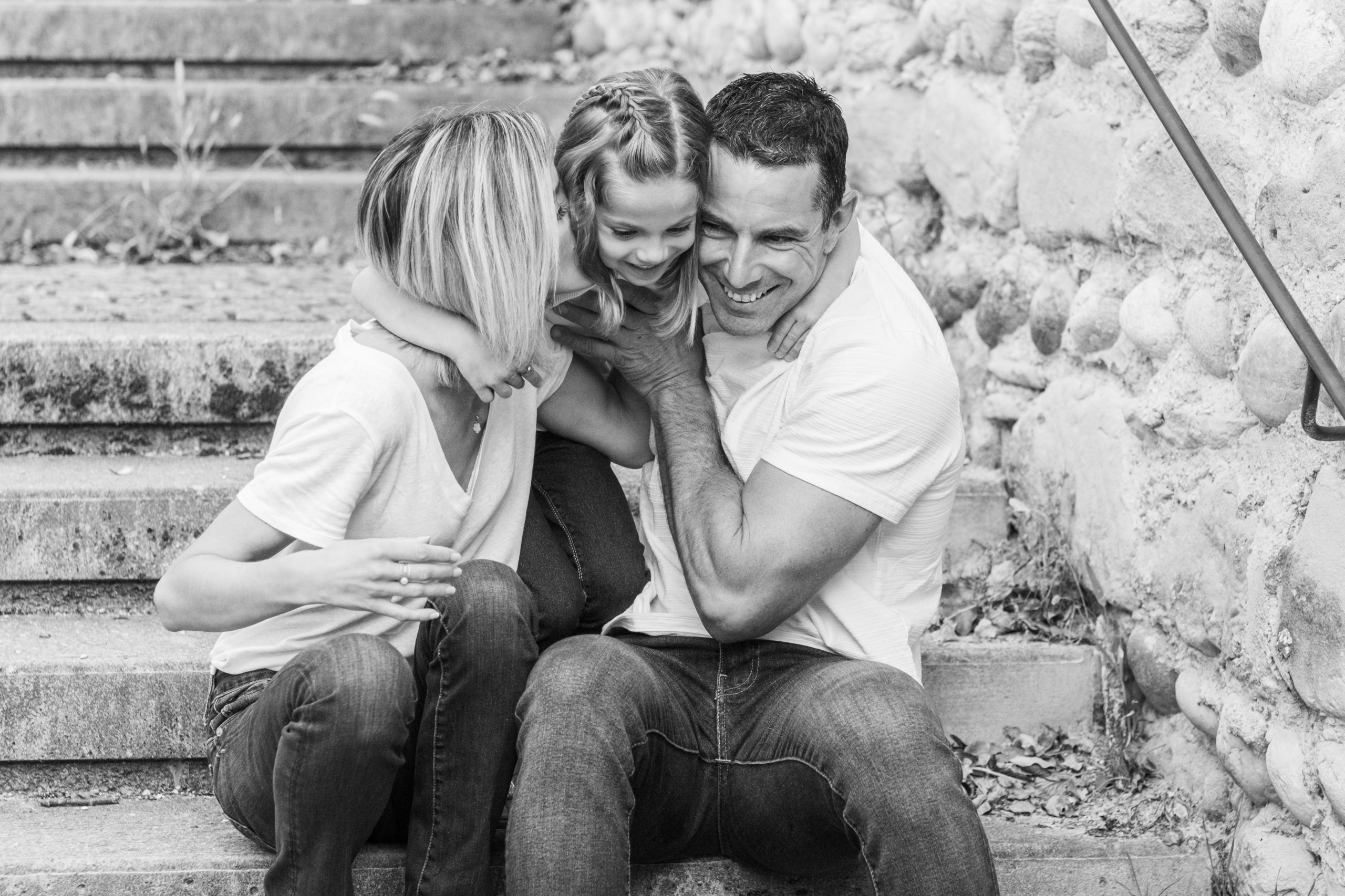 parents et leur fille enlacés sur des marches en pierre, photo de famille en noir et blanc