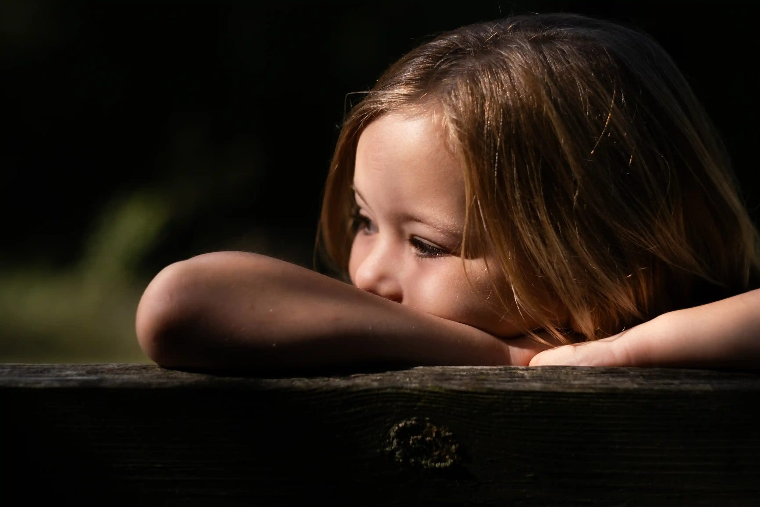 portrait d'une petite fille accoudée à une barrière en bois, regard rêveur, photographe famille en Drôme
