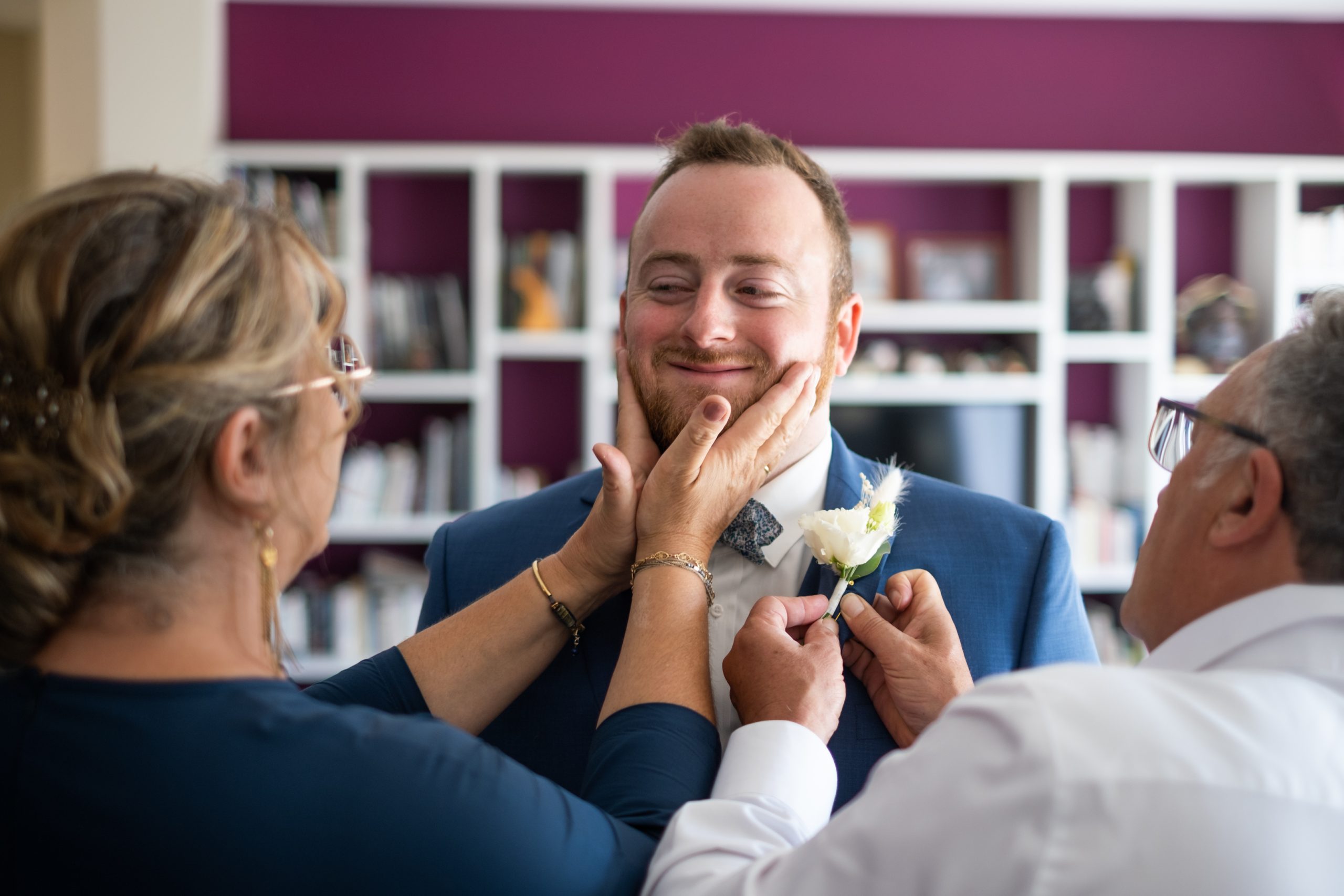 La maman du marié lui prend le visage dans les mains pendant que son papa ajuste la boutonnière