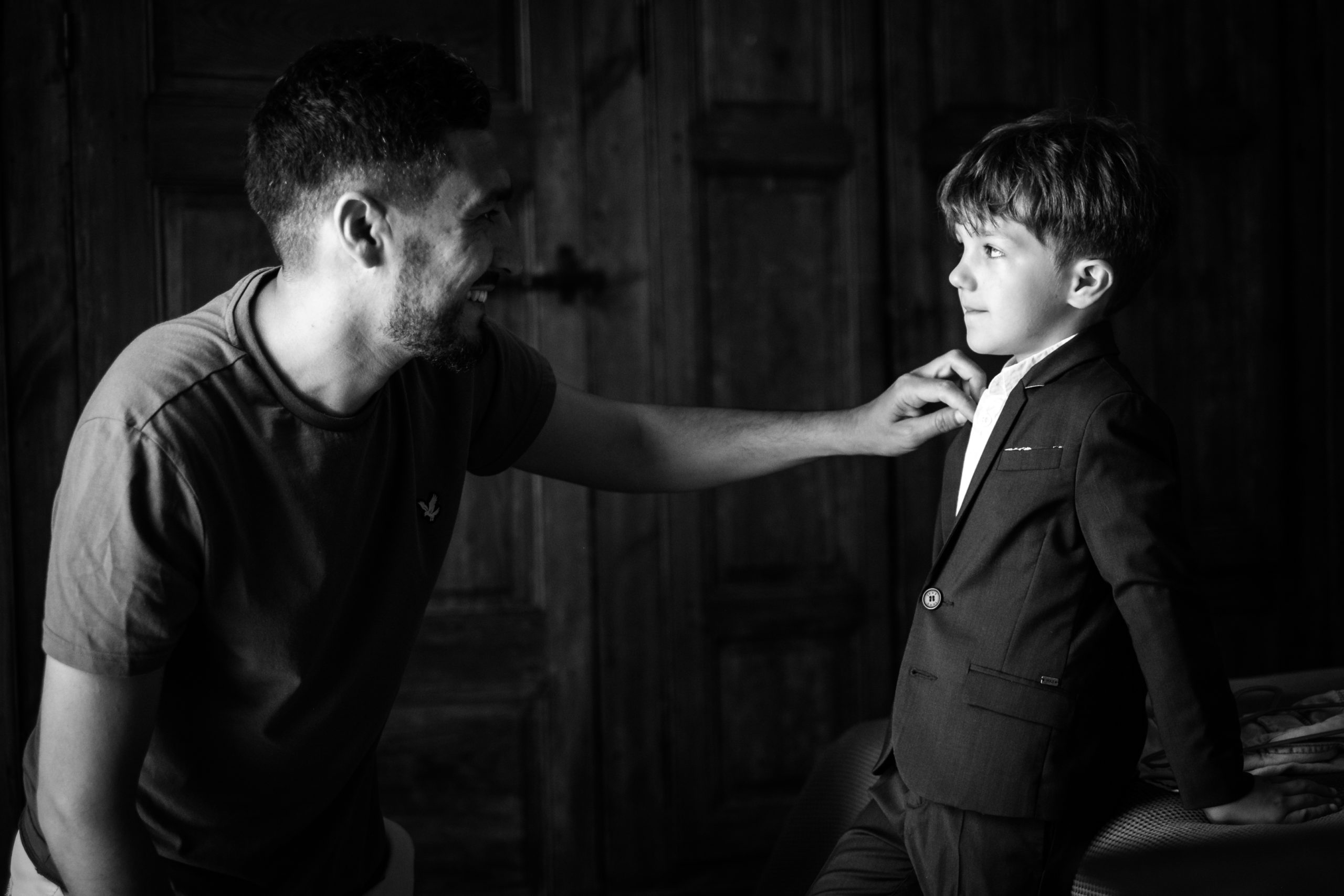 Un papa ajuste le col du costume de son petit garçon pendant les préparatifs du mariage