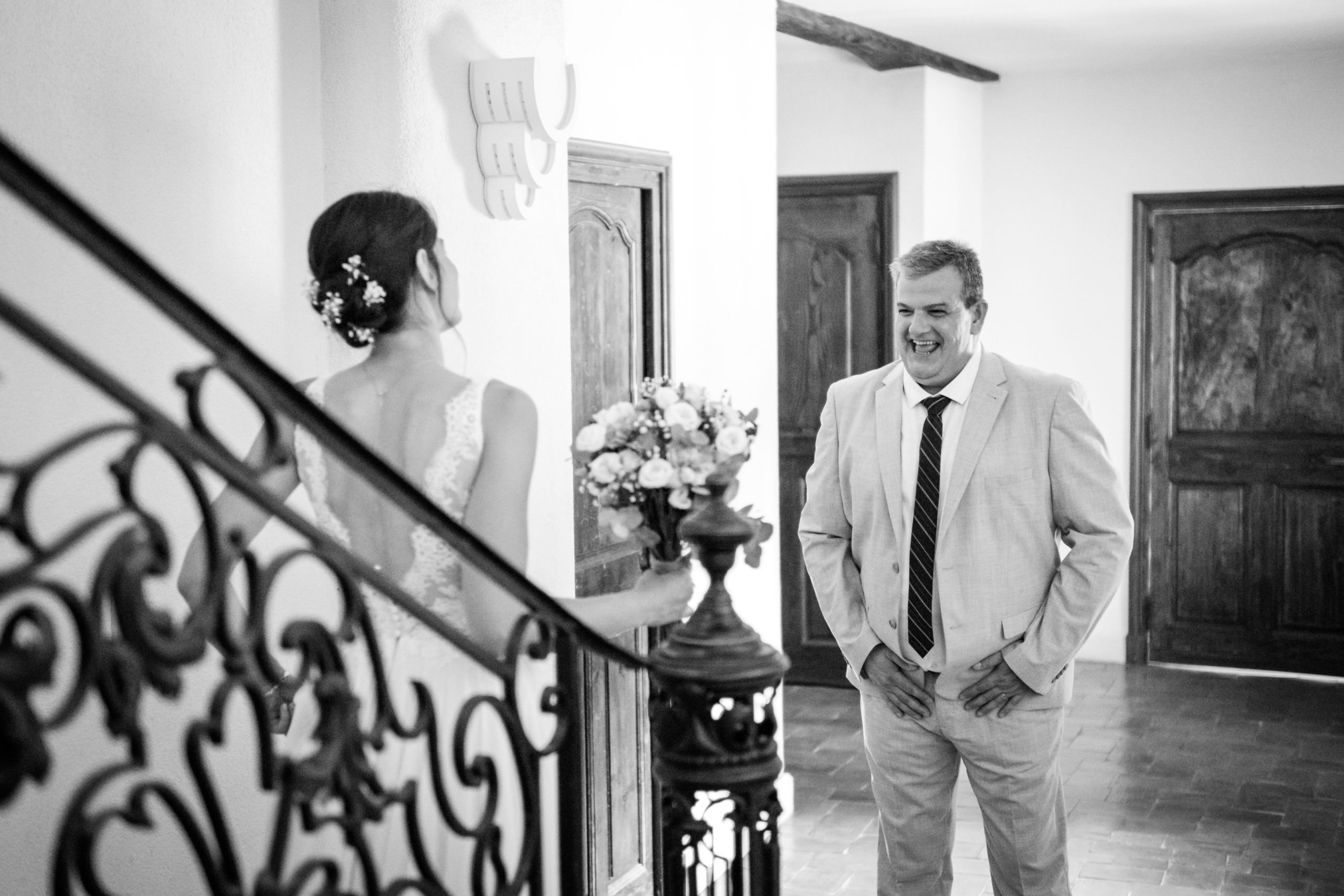 Le papa découvre sa fille en robe de mariée au pied de l'escalier, sourire aux lèvres
