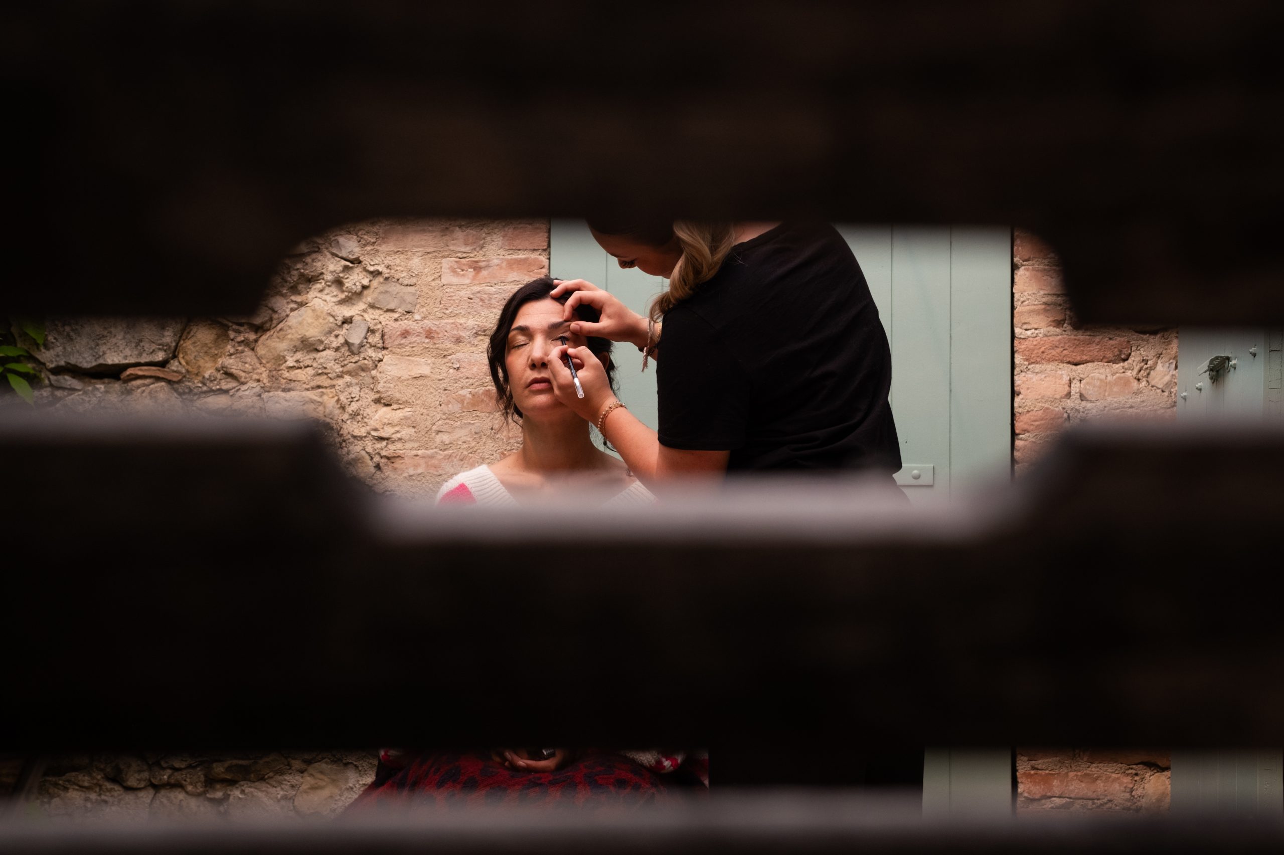 Maquillage de la mariée photographié à travers une ouverture dans un volet, préparatifs de mariage en Drôme