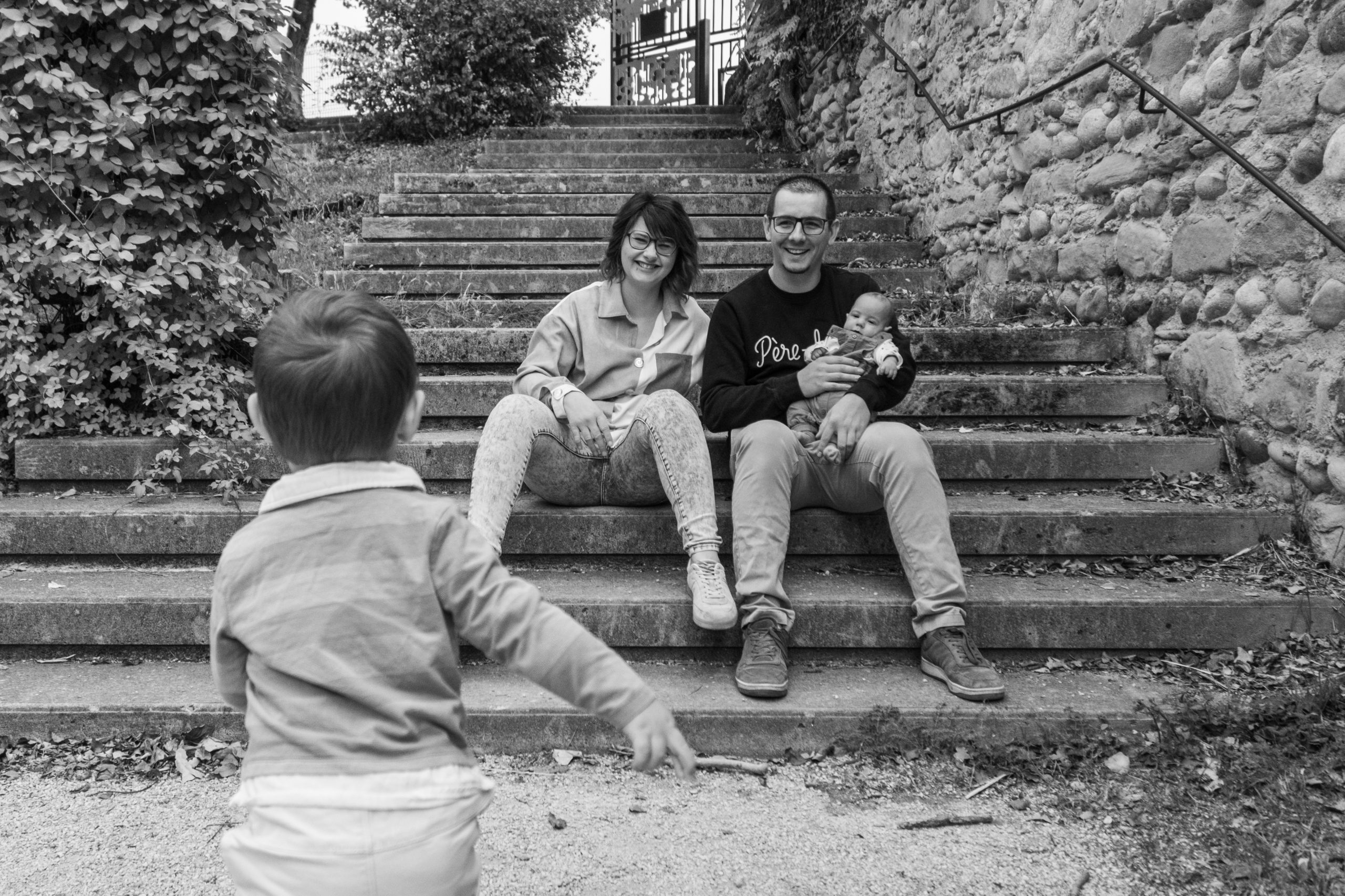 famille assise sur un grand escalier en pierre en ville, séance photo famille en noir et blanc, photographe en Drôme
