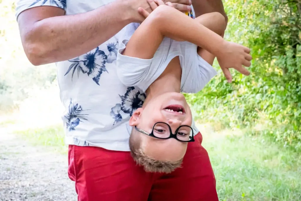 Enfant qui rit la tête en bas pendant une séance photo famille en extérieur